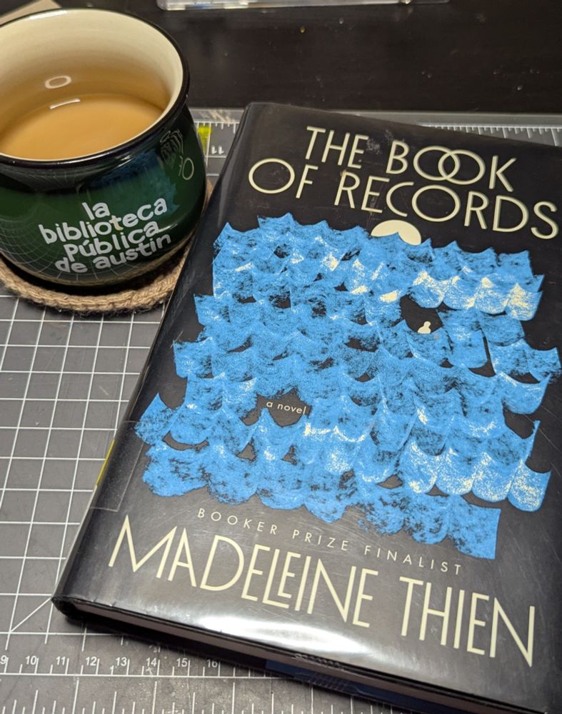 Cup of coffee in an Austin Public Library mug and the book The Book of Records by Madeleine Thien.