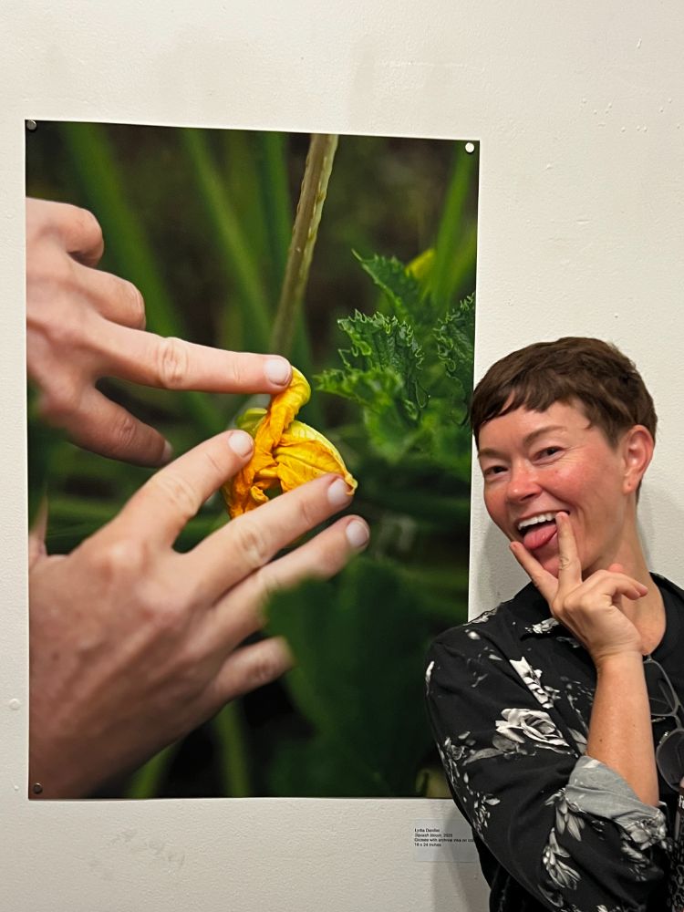 Making a sexy tongue gesture in front of a photo of hands gently spreading open the petals of a zucchini blossom.