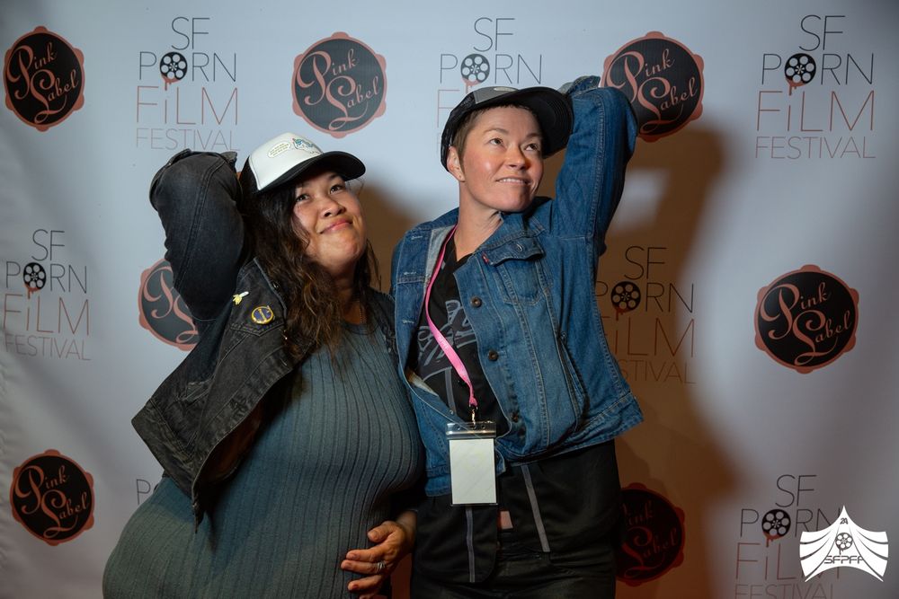 Rae Threat and Jiz Lee pose in hats by AP Clips at the 2024 San Francisco Porn Film Festival