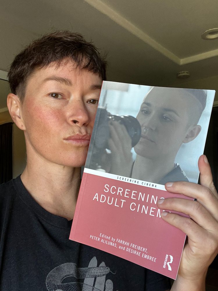 Jiz Lee poses with the book Screening Adult Cinema which features Jasko Fide caressing a camera lens. 