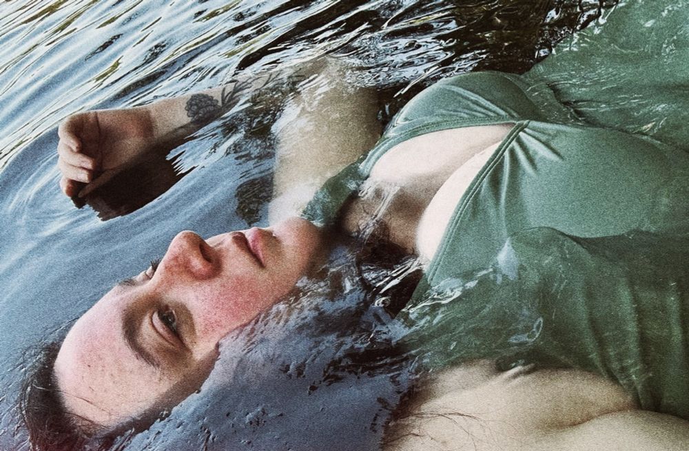FTR floating in the dark waters of a northern lake. She’s wearing an olive green a thing suit. 