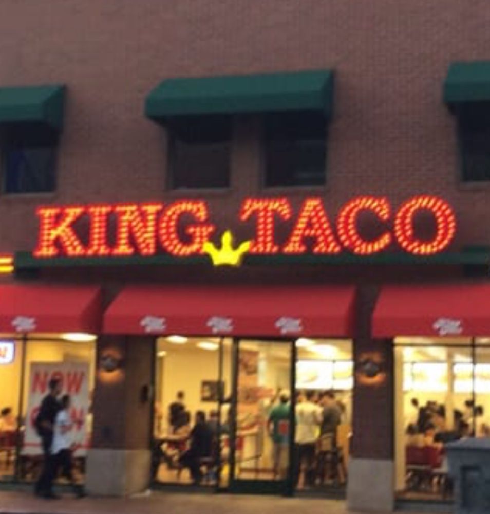 Building facade with illuminated “KING TACO” sign above restaurant entrance.