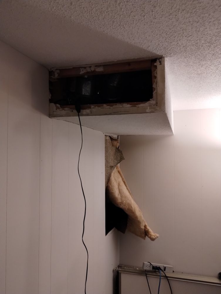 Before, earlier: ceiling bulkhead with vertical end removed.

The wood framing is visible, as are bits of drywall edges nailed to frame.

Some duct work is barely visible in the revealed space.

A cord runs to a small light that is shining out of sight in this image 

A hole on the wall is visible where roommate removed some paneling earlier. Insulation is sticking out.