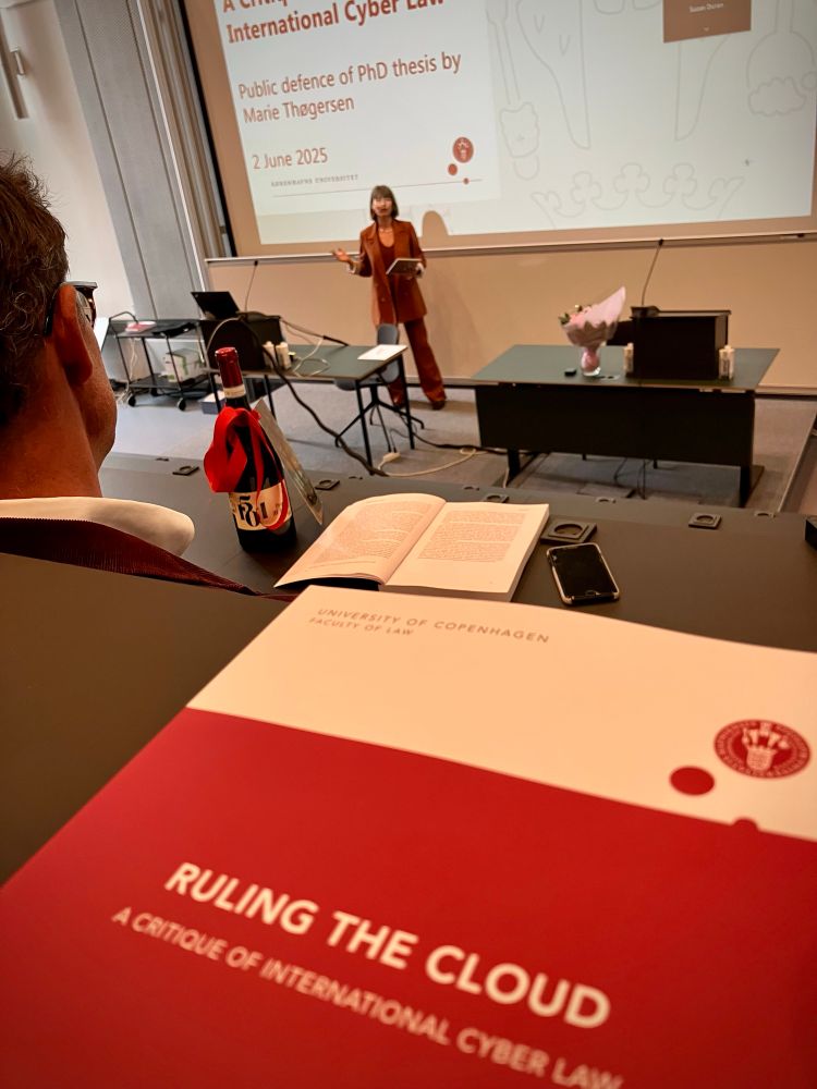 Marie Thøgersen’s PhD thesis, “Ruling the Cloud”, in the foreground with her in the background defending the thesis.