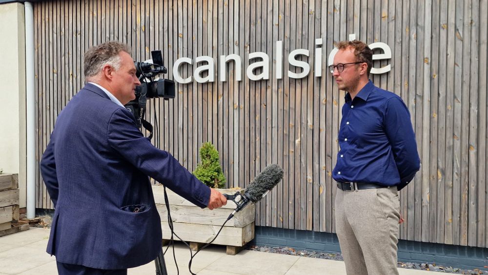 Adam Dance MP being interviewed outside the Canalside building, speaking to a TV reporter holding a microphone, with a camera set up to film.