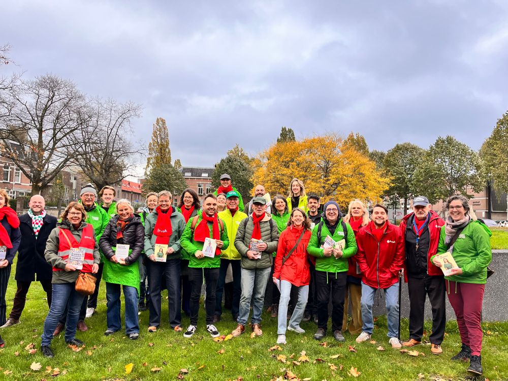 Grote groep vrijwilligers van GroenLinks en PvdA in groene en rode jasjes, met verkiezingsflyers in de hand. 
