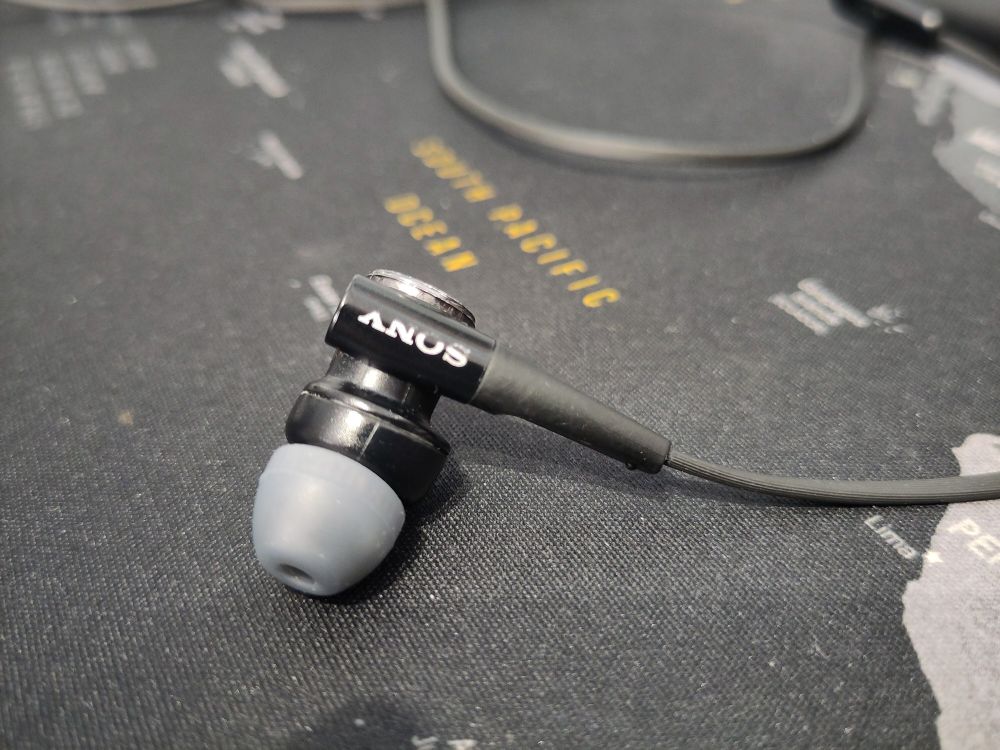 Sony headphones lying on a table. The bottom part of each letter is worn off, which results in the word "Anus" when read upside down.