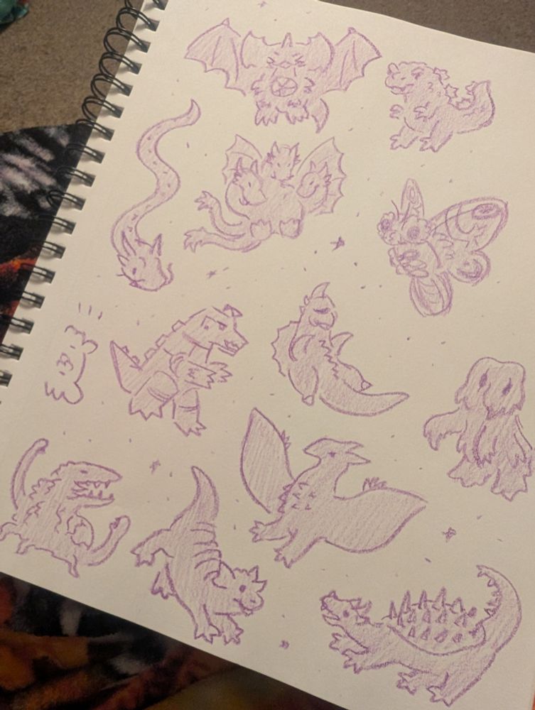 A photo of a sketchbook page filled with godzilla kaiju drawn in a simple style using a purple crayon