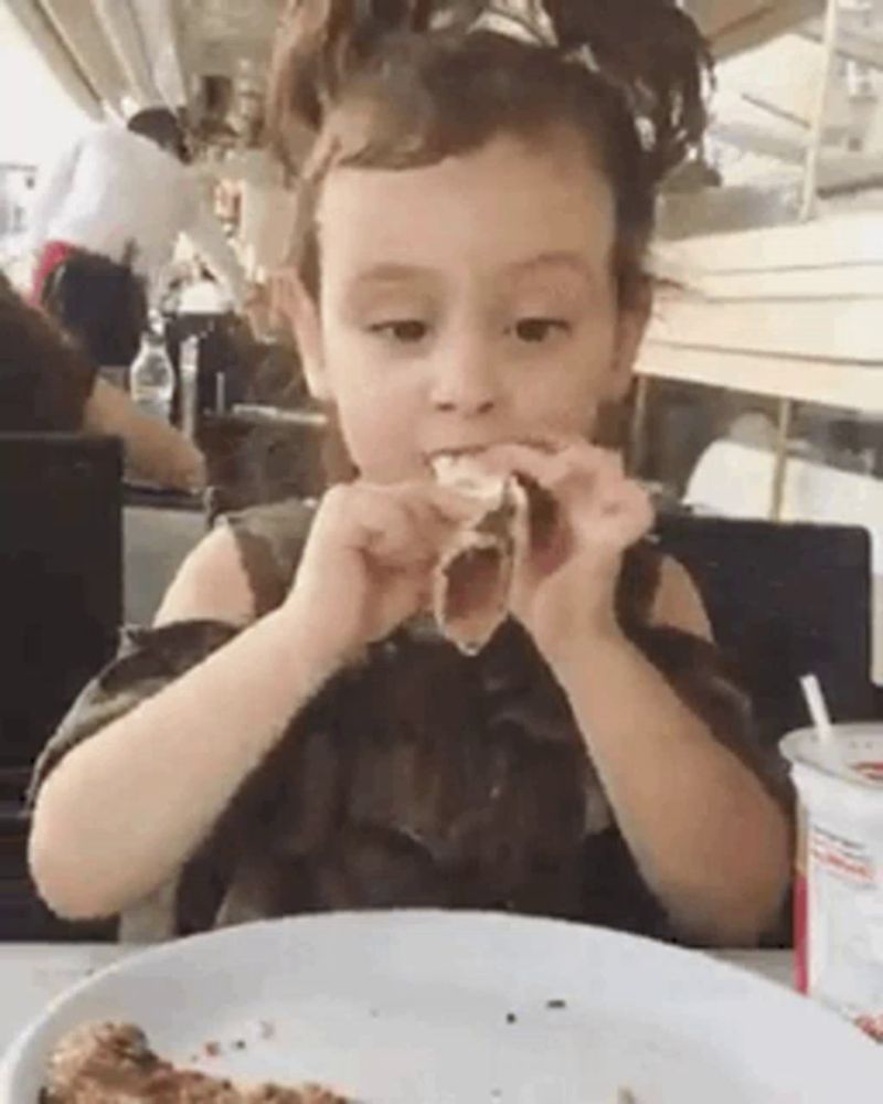 a little girl is sitting at a table eating a slice of pizza .