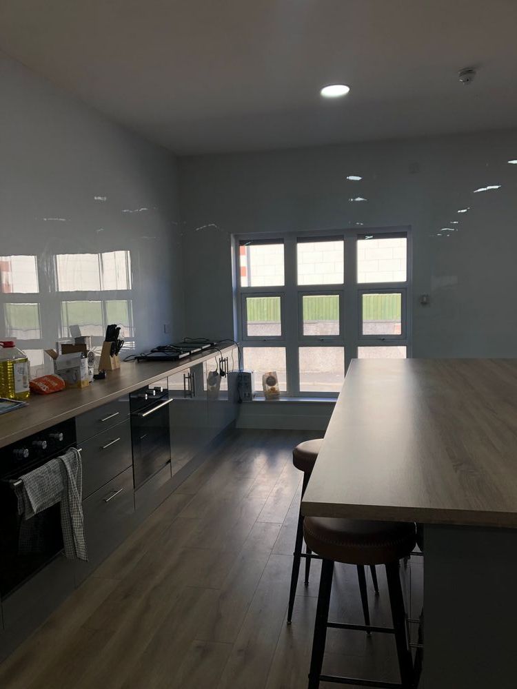 A photo of a large kitchen counter and island with windows at the end of the room. There are bar seats at the island and hobs and ovens as part of the counter.