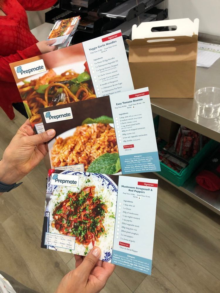 A pair of hands holding three prepmate recipe cards, which have a title, photograph, and ingredients list.