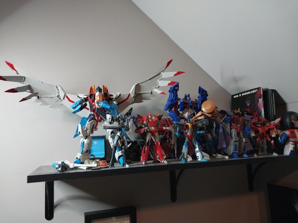a collection of tranformers figures on a shelf. there are six starscreams, one knockout, an ultra magnus, and the spines of various books and comics vosible behind the figures.