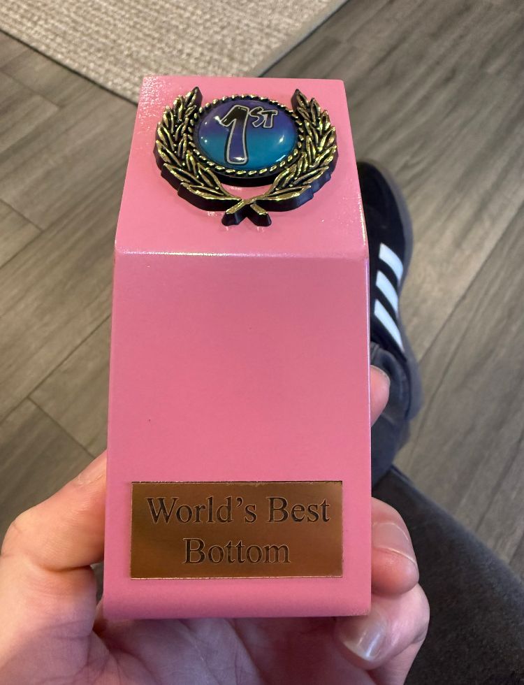 Picture of a hand holding a pink trophy. The trophy reads “world’s best bottom” at the base and has a blue #1 at the top