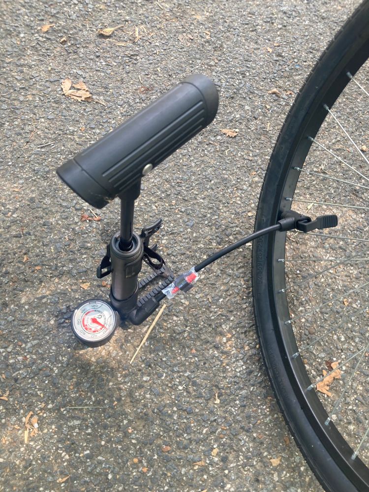Picture of a bike pump connected to a wheel on the pavement. 
