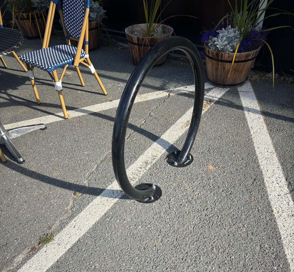 A single bike parking ring sits outside of a cafe. Patio chairs and planters are adjacent.