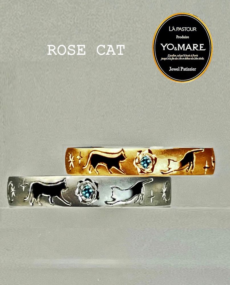 ブルーダイヤモンドが留まるバラの模様の両サイドにねこの模様が遊ぶ、ゴールドとプラチナのペア・結婚指輪オーダーメイド作品