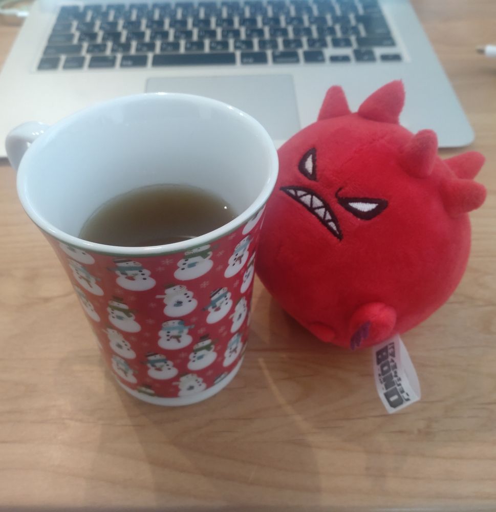 赤地に色々な衣装を着た雪だるまの模様のマグカップに入ったお茶とビーストくん。