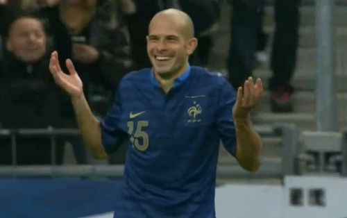 L'ancien joueur de l'équipe de France de foot Christophe Jallet, souriant et en haussant les épaules et les bras de surprise après son but venant d'un centre raté 