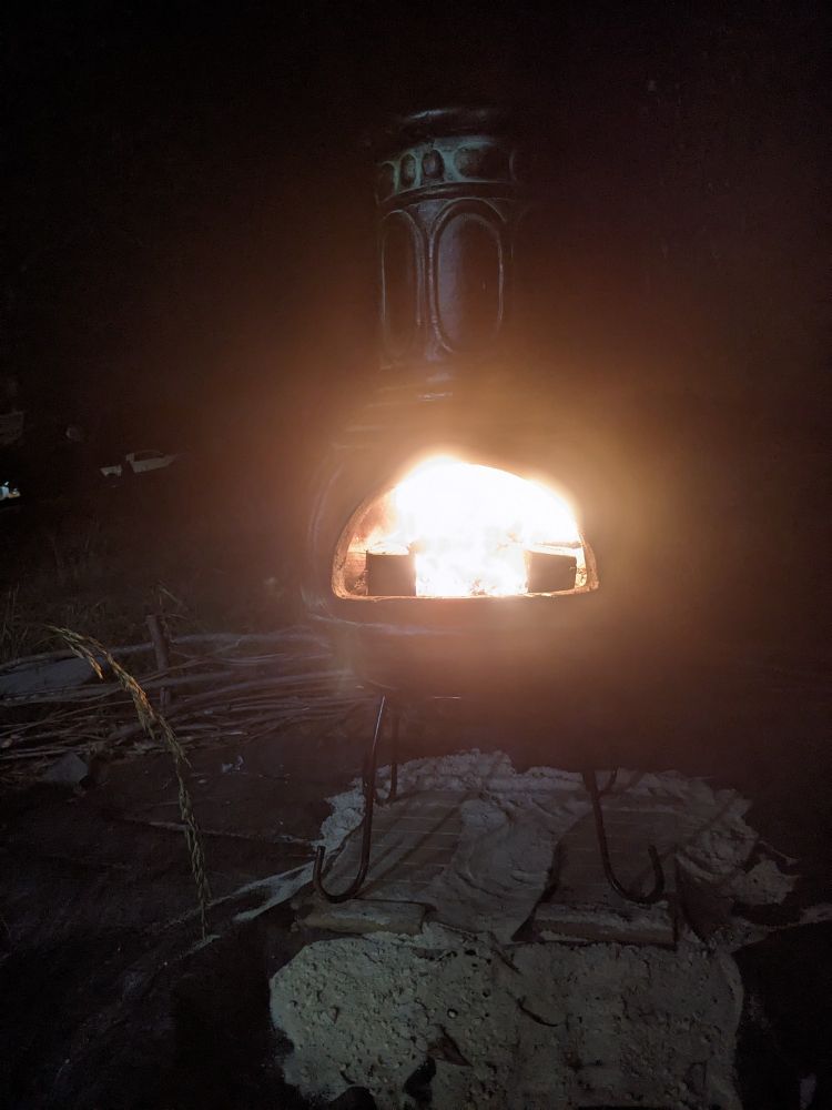 An outdoor chimney at night.  Orange flames bathe the darkness in bright light.