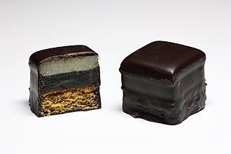 Weißer Hintergrund, darauf sind zwei Lebkuchenpralinen, Dominosteine, eins ist durchgescnitten.