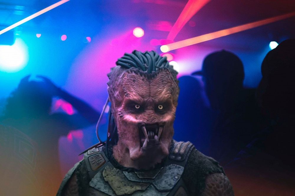 Predator from Predator: Badlands superimposed over a club scene to look like they're in a club