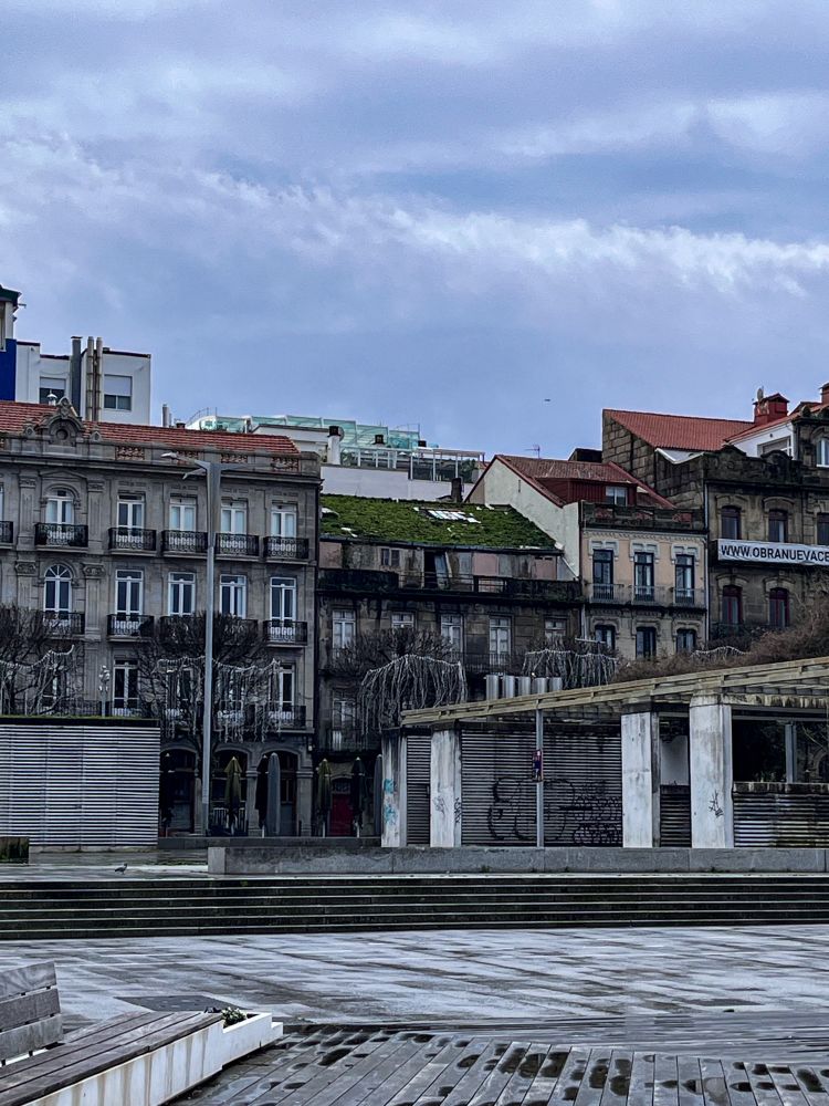 Edificios de Montero Ríos, en Vigo. Están mojados por la lluvia y el del centro tiene el tejado cubierto de verdín y está muy deteriorado. El cielo está nublado y la estampa es bastante gris, tanto literal como metafóricamente.