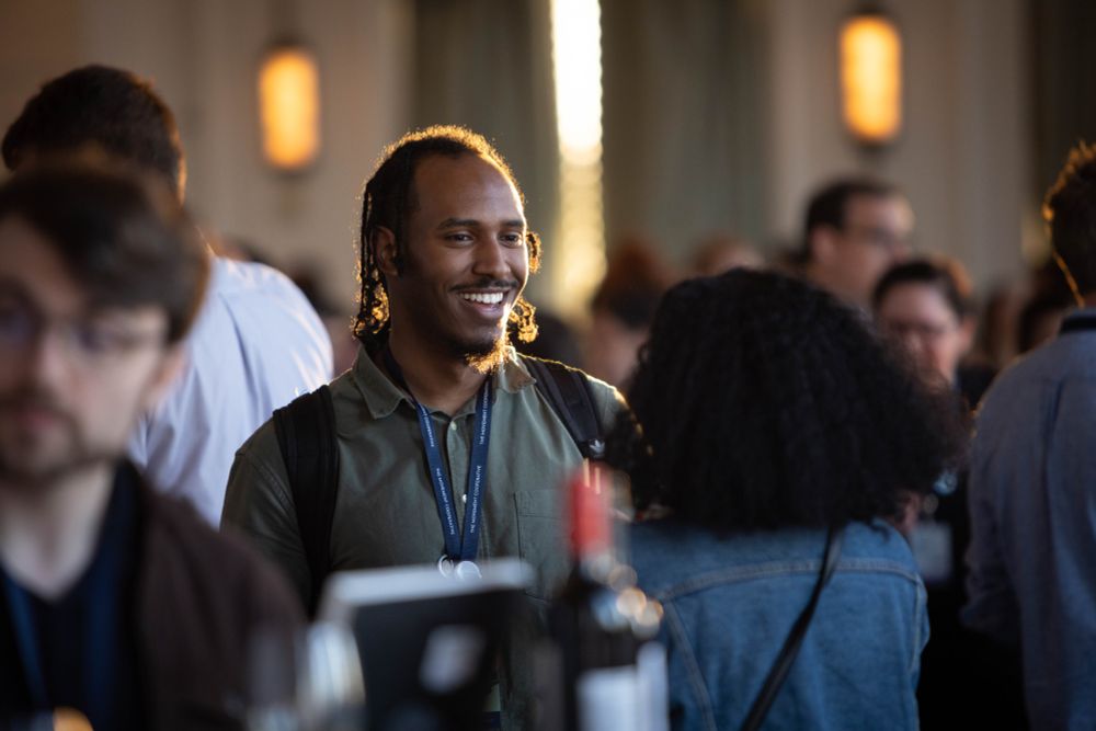 Attendee smiling while talking with someone, surrounded by a standing group at TMC’s The Movement Conference 2023 in St. Louis, MO.