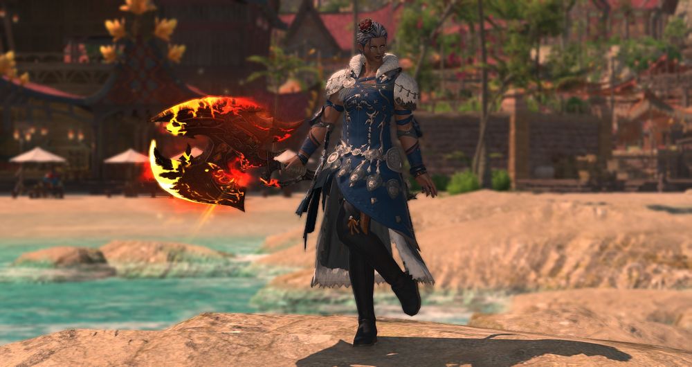 A Hellsguard Roegadyn Warrior standing on the beach in Tuliyolal. She wears a long blue coat, decorated with silver ornaments. The shoulder pads, collar and trim are covered in a fluffy white material. She wears a set of rings and bracelets on her hands, and blue longboots on her legs. A small crown sits tilted on her head.