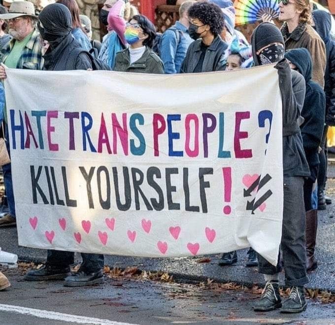 Masked protestors (pride attendees?) holding up a banner which reads, "Hate trans people? Kill yourself!"