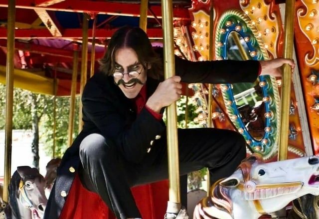 Matt Mercer dressed evily, riding carousel