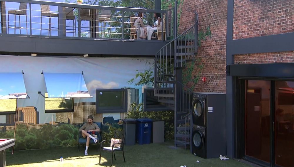 a wide shot of the BB back yard showing Rachel and Ashley sitting close together on the upper balcony while Vince sits alone below them.