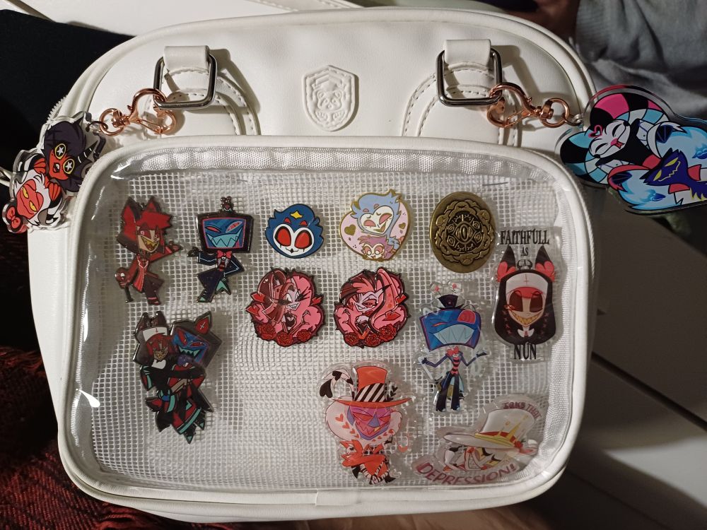 My Ita bag with 12 pins and 2 keychains. They are all hellaverse related. Theres Alastor, Vox, Stolas, Lucifer, Valentino, Octavia, M&M, Ozzie and Fizz