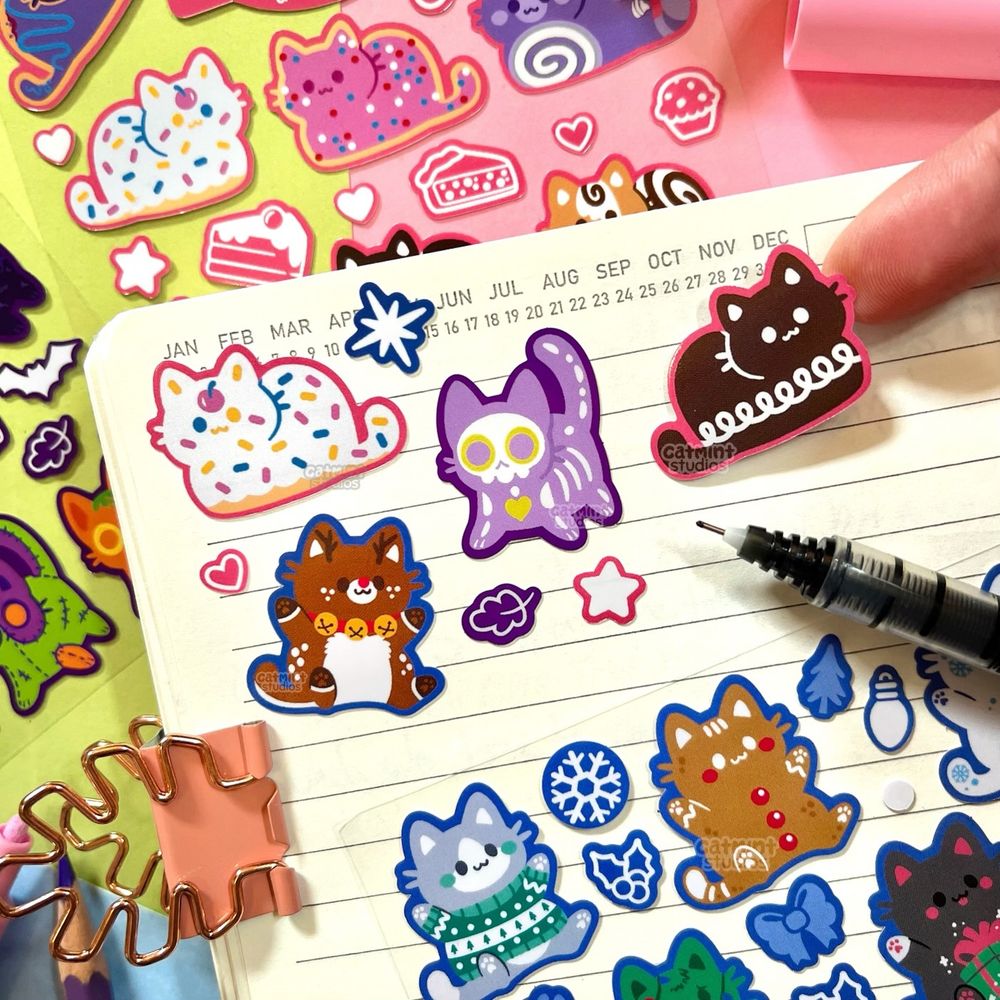 Assorted cat stickers on a notebook page. They are themed around desserts, holiday vibes, and Halloween. 