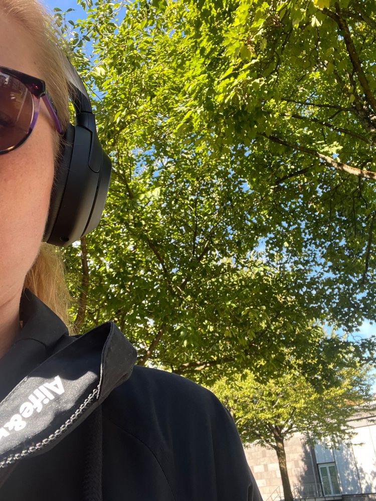 Ein kleiner Teil meines Kopfes mit Sonnenbrille und Kopfhörern. Daneben Bäume in der Sonne und ein wenig blauer Himmel.