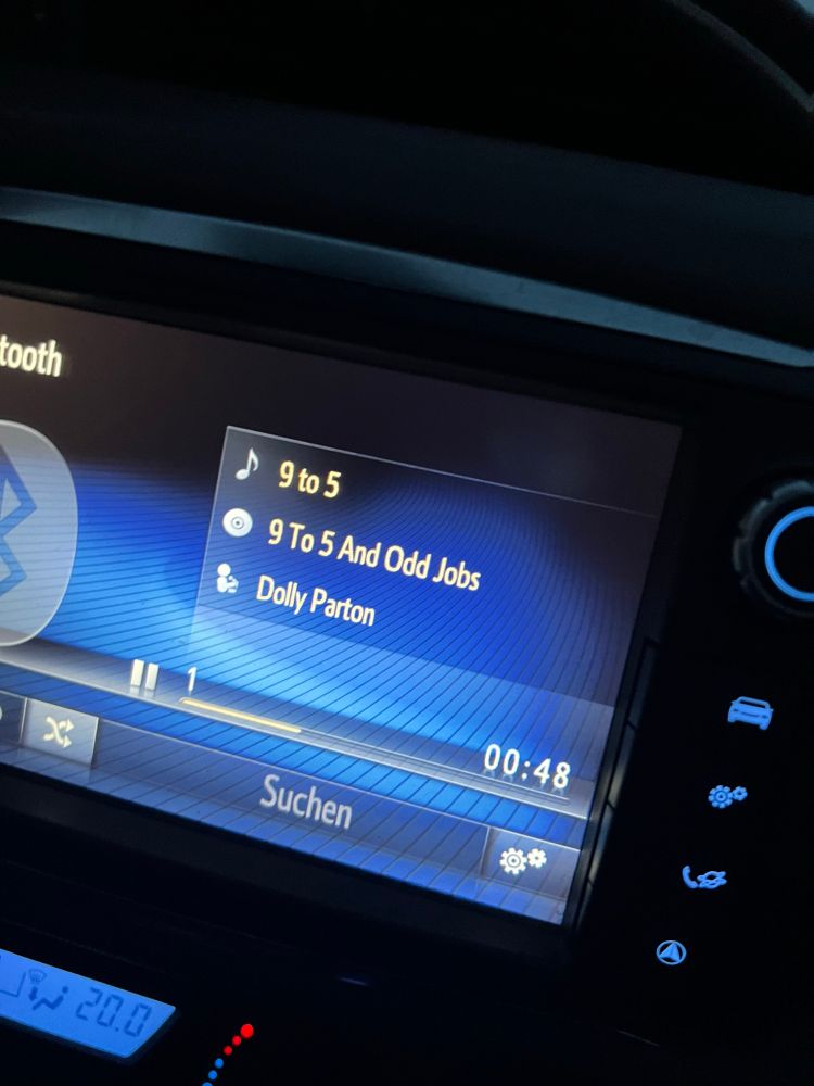 Foto der Anzeige des Autoradios. Es läuft 9 to 5 von Dolly Parton.