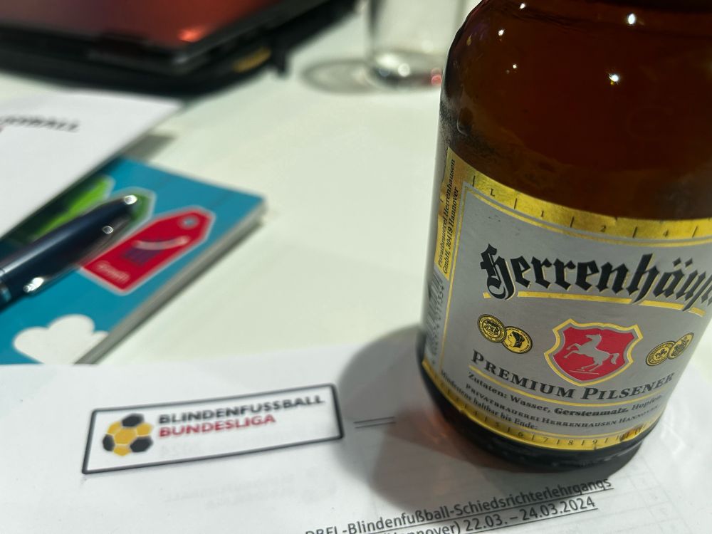 Eine Flasche Herrenhäuser und Notizzettel mit dem Blindenfußball-Logo.