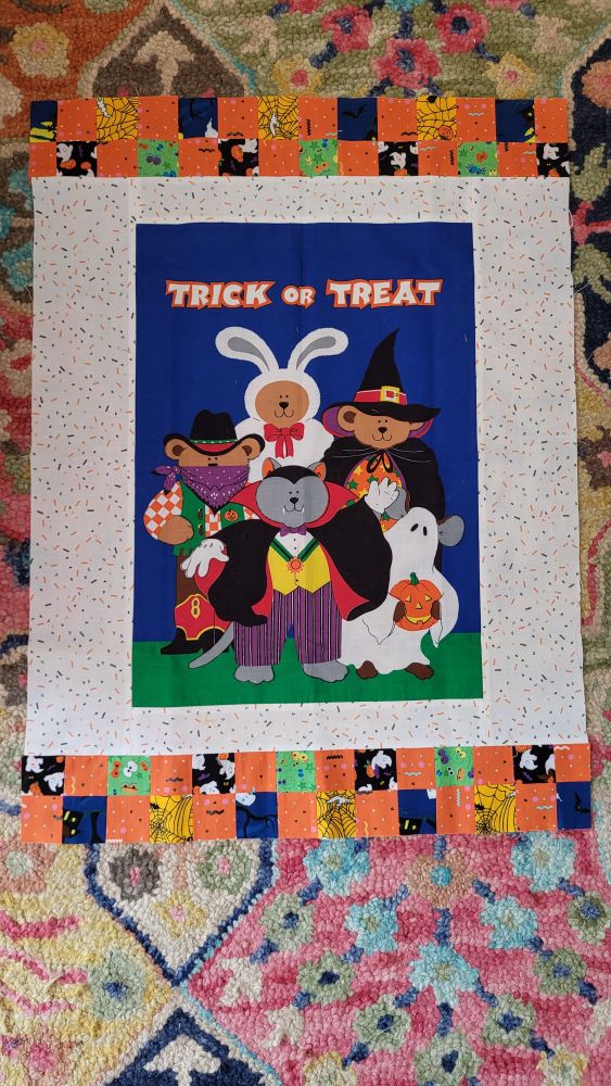 unfinished quilt top with a vintage 90s panel in the middle of little animal giys dressed in halloween costumes that says "trick or treat!". the panel is bordered by white and then a row of smaller 4 square squares in different halloween prints
