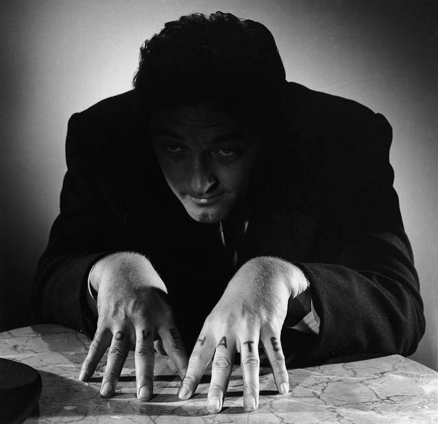 scene from night of the hunter. The reverend has a menacing look in his eyes, showing off his iconic “LOVE” and “HATE” finger tattoos 