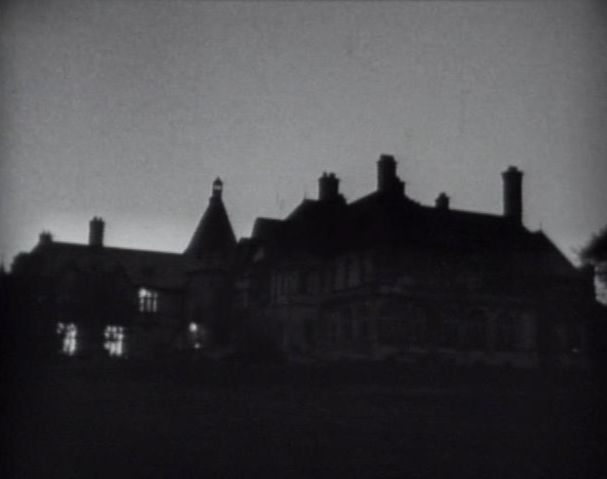 A large mansion (Collinwood) silhouetted against the night sky. A few lights can be seen in the windows.