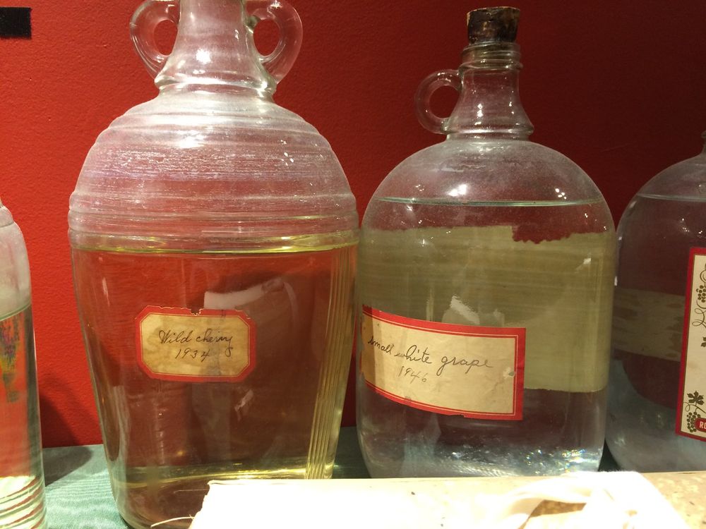 two galloon jugs of clear liquor, one labled "Wild Cherry 1934" the other "Small White Grape 1946"