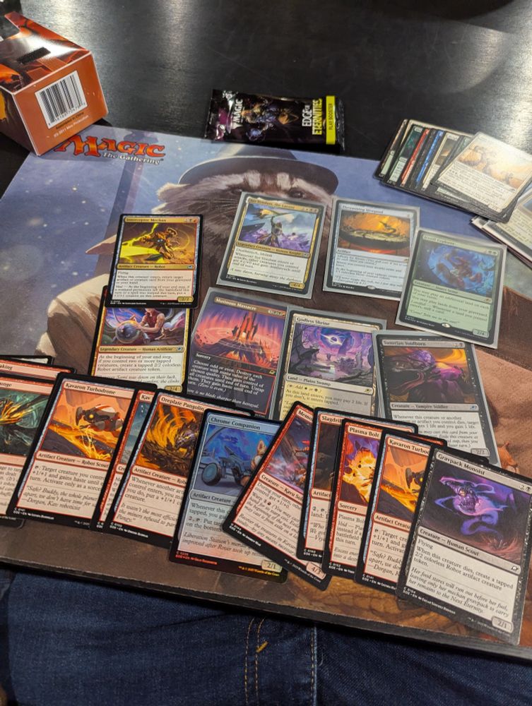 Magic cards are splayed across a playmat. They are mostly red or black with a few white, multicolor, and green ones.