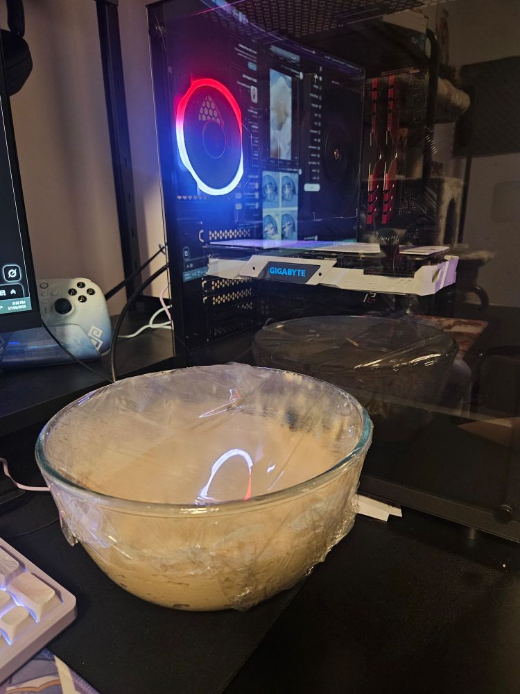 Large bowl of proofing dough sitting on a desk next to a PC tower