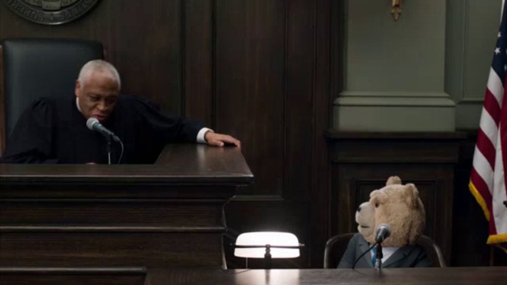 a teddy bear sits in front of a microphone in a courtroom