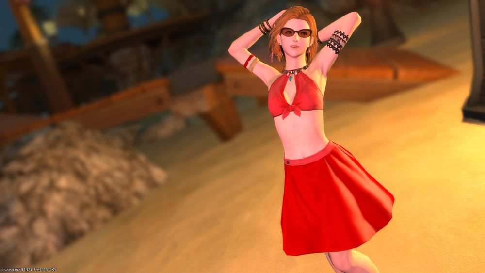 Amber Kleveton in a red swim top and red mini skirt with orange sunglasses. Her hands behind her head. Posing on the beach.