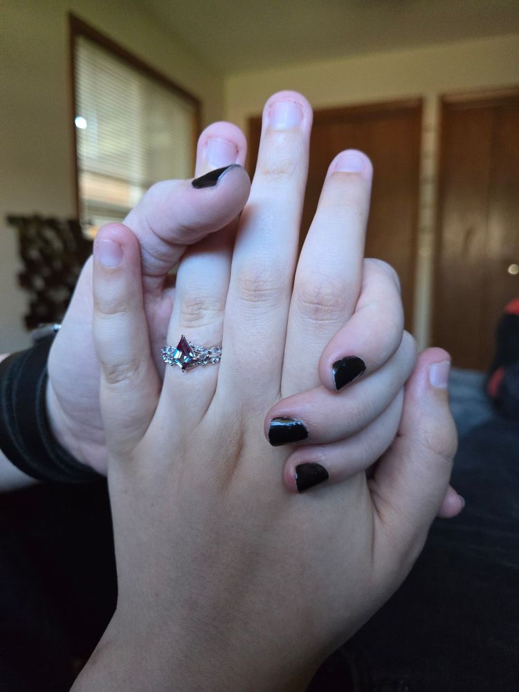 N-311 is holding her fiancée's hand.  Nell has a new engagement ring, featuring a kite-cut alexandrite.