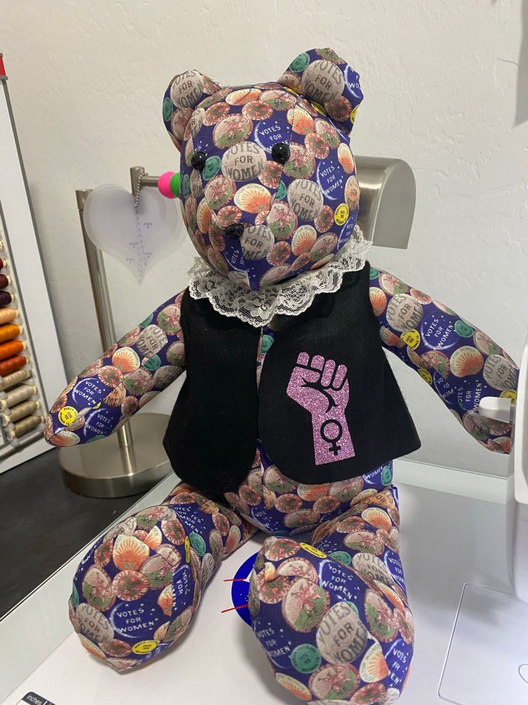 Teddy bear made from 1915 suffragette, votes for women buttons, fabric.  Has RBG robes and white collar.  Nods to Susan B Anthony and RBG and women’s rights. 