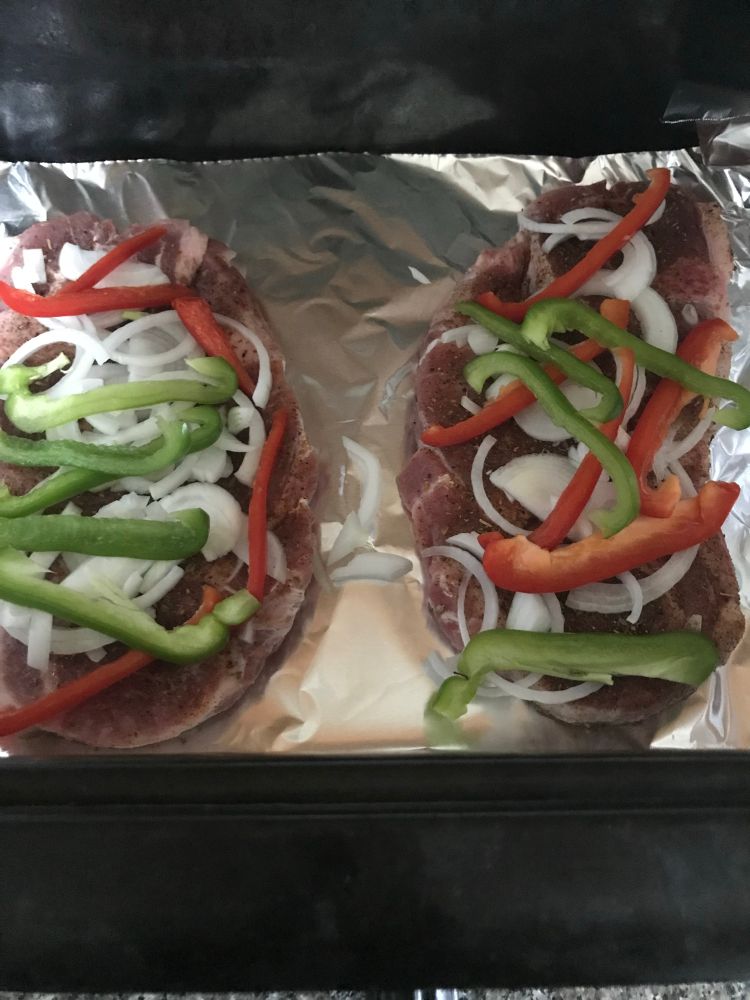 Raw steaks covered in peppers before being cooked. 