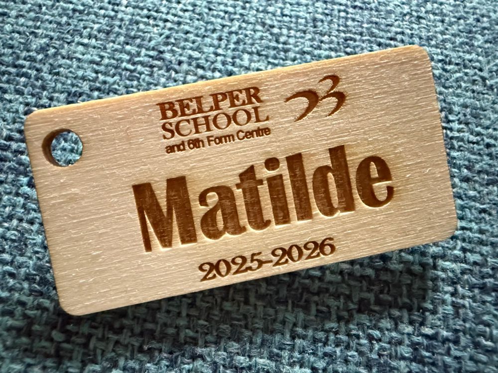 Wooden name badge with the name Matilde and school logo on it. 