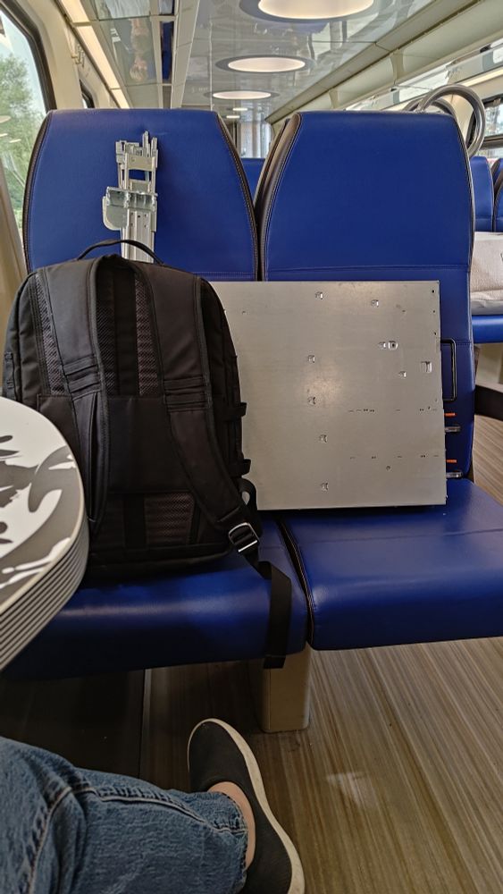 photo of server lying across two seats on a train, and a backpack with some server rails