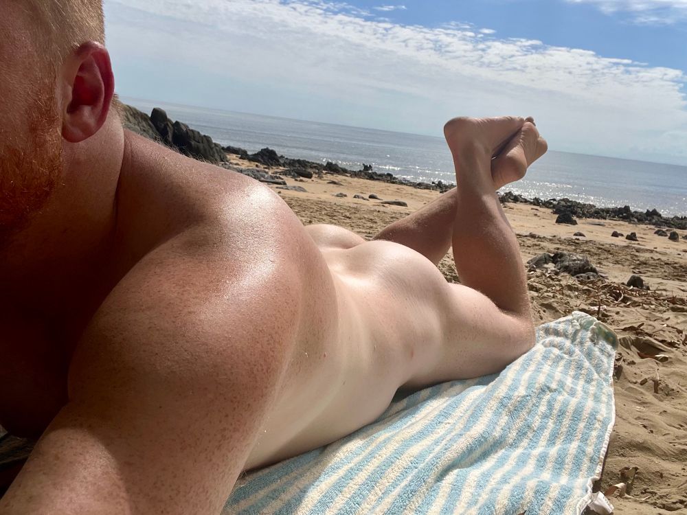 Ginger man nude at the beach lying on his stomach on his towel with butt on display 